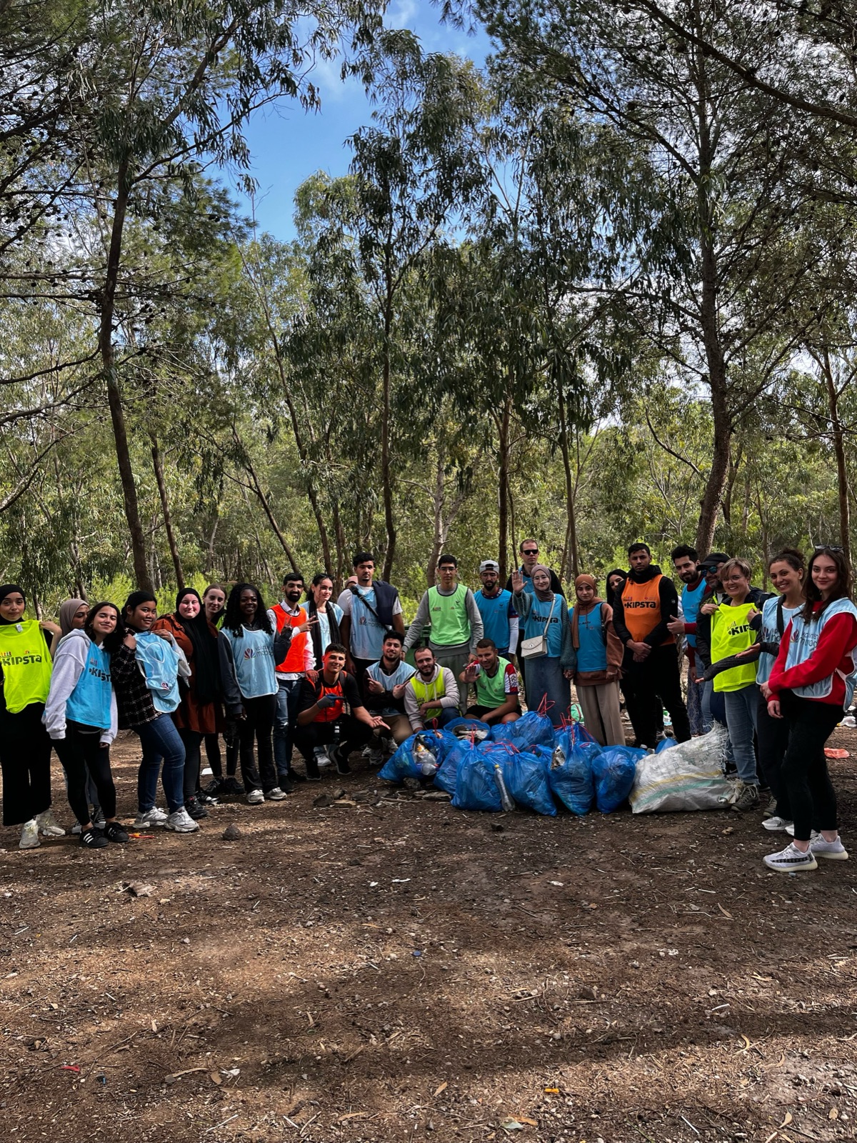 A group of people posing outdoors in a forest with bags of collected waste.