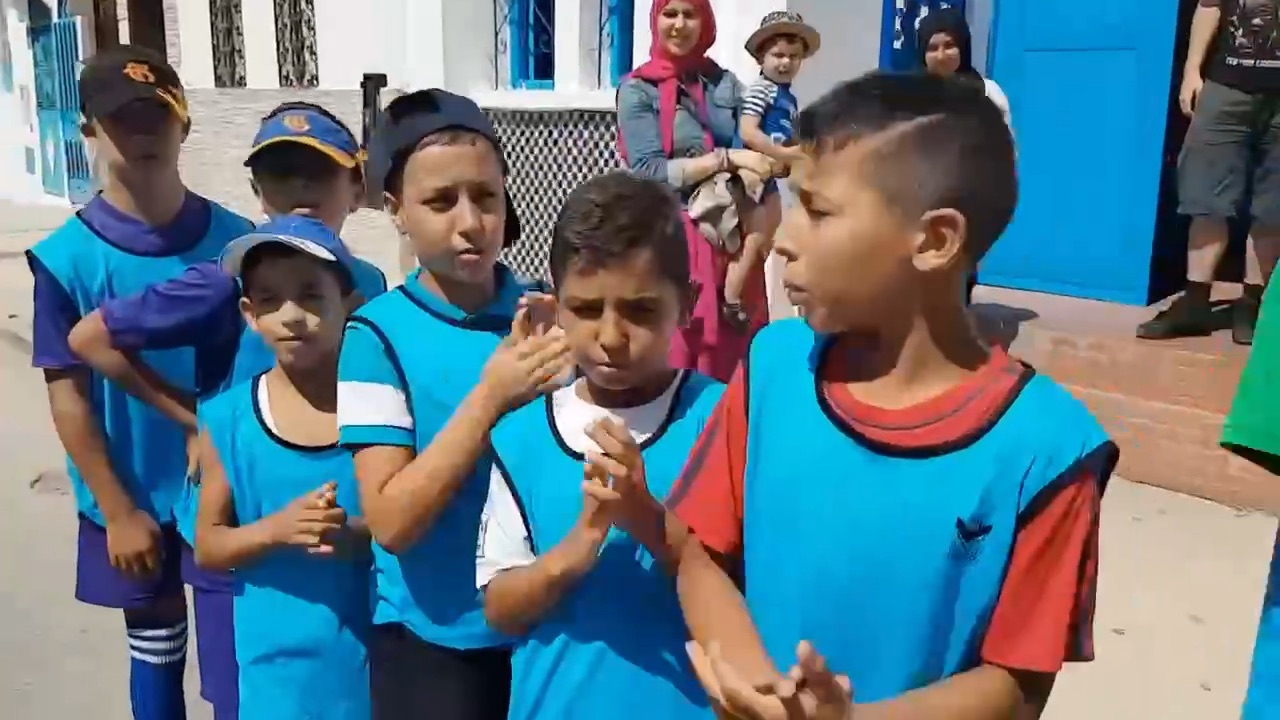 Children in sports bibs clap and sing during Project Yatra